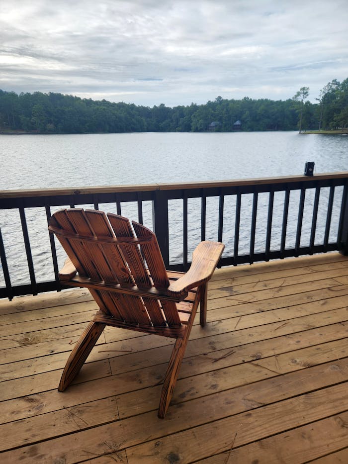 Peaceful view of a lake with an Adirondack chair on a wooden deck. Perfect relaxation spot.
